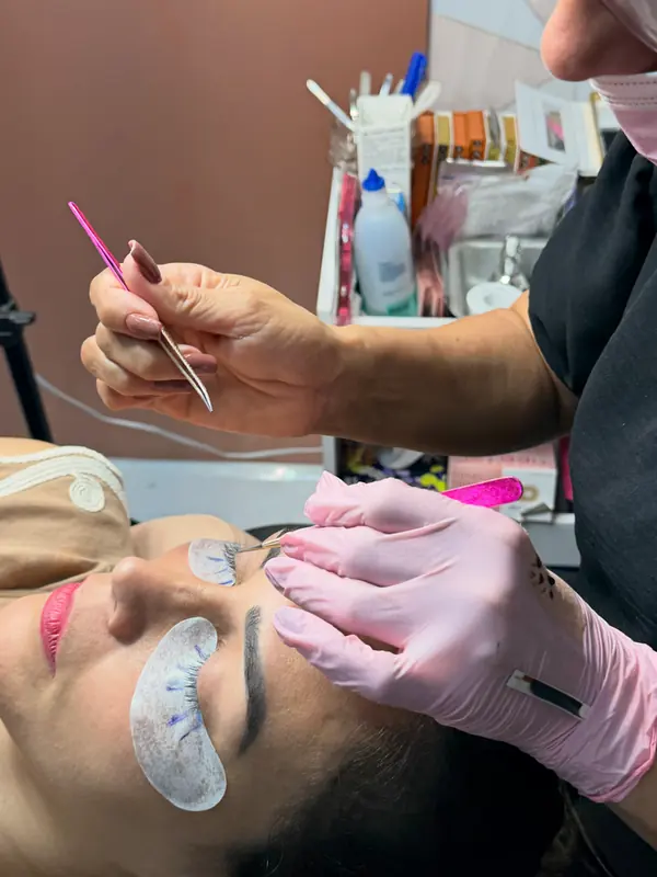 Profissional de luvas aplicando extensão de cílios com pinça, fio a fio