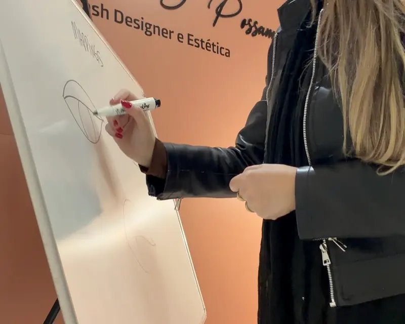 Ana Paula desenhando o mapeamento de cílios num quadro, durante um curso